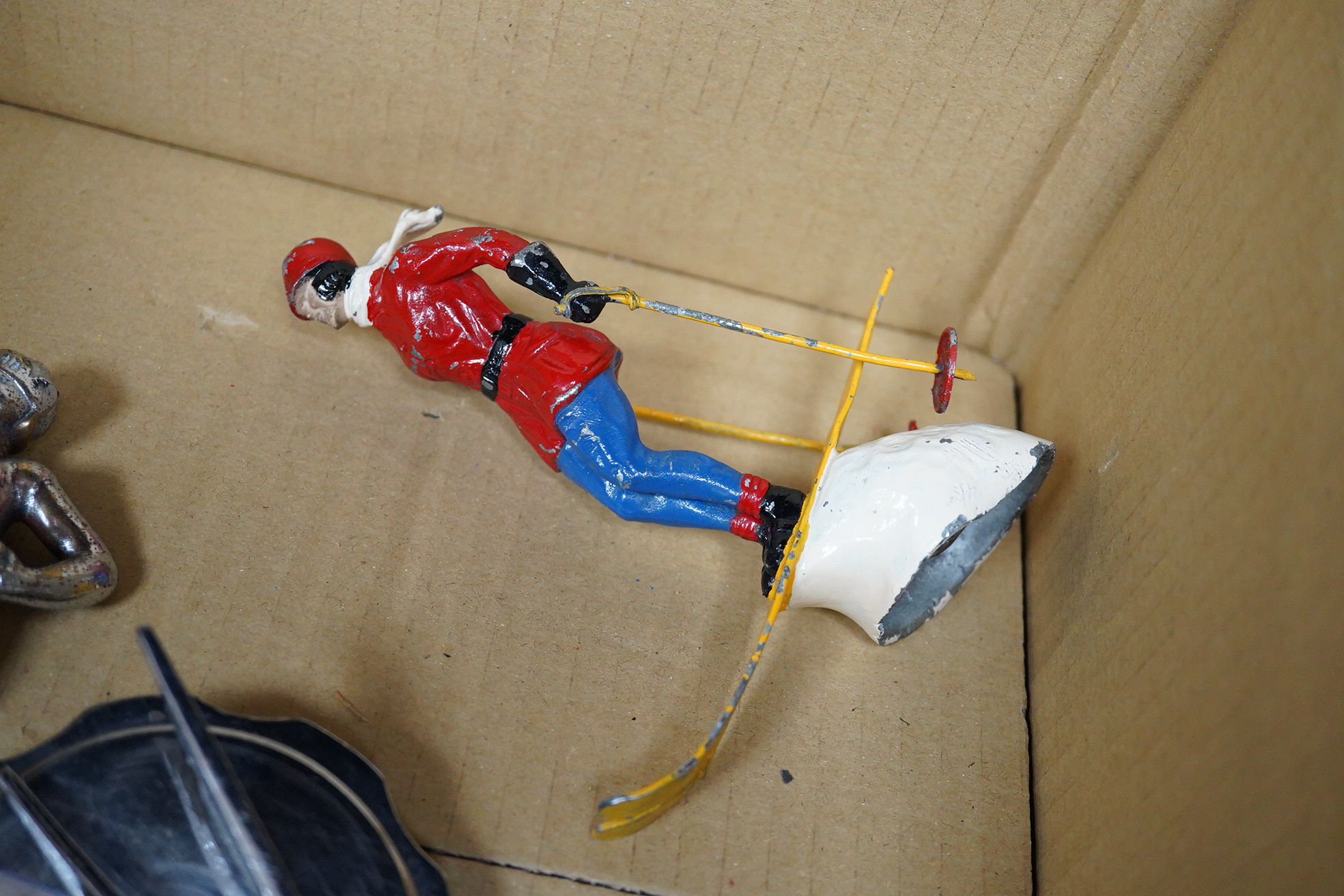 Six car mascots including five chrome and brass examples; a female figure, a cherub with harp, an Art Deco winged figure, etc. and a cold painted spelter figure of a skier